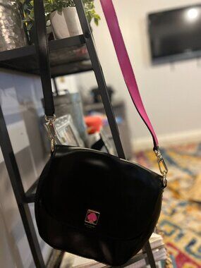 Kate Spade New York black crossbody bag with pink strap detail.